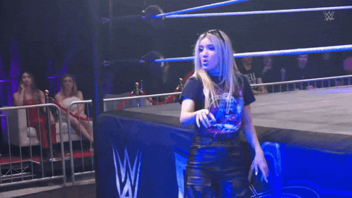 a woman in a wrestling ring with a w logo on the wall behind her