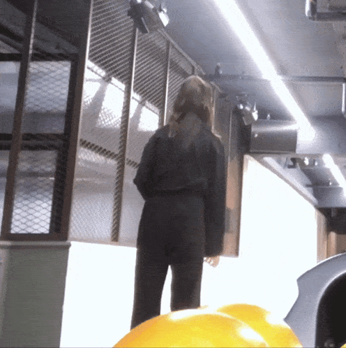 a woman in a black jumpsuit stands in front of a wall
