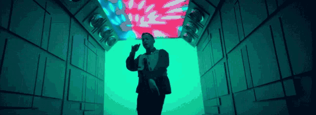 a man in a suit is standing in a hallway with a green light behind him