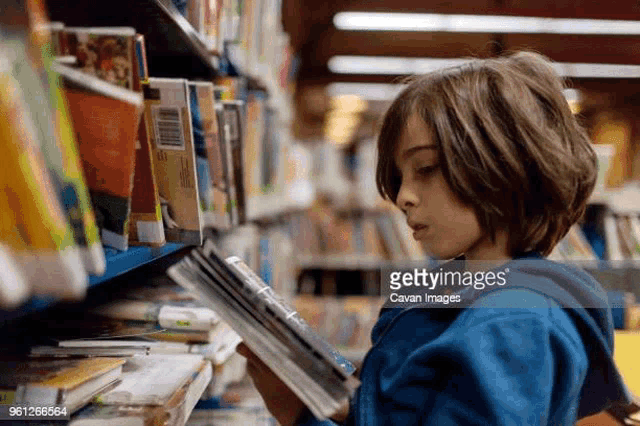 a boy is reading a book in a library .