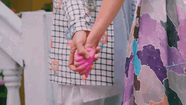 a man and woman holding hands with a pink heart in their hands