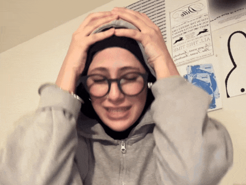 a woman wearing glasses and a hijab holds her head in front of a sign that says vit