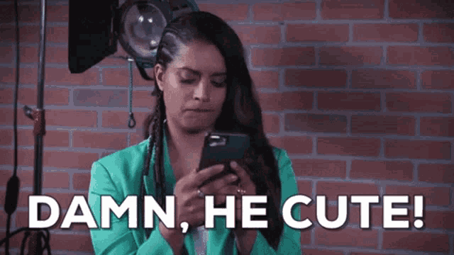 a woman in a green jacket is looking at her phone and says damn he cute