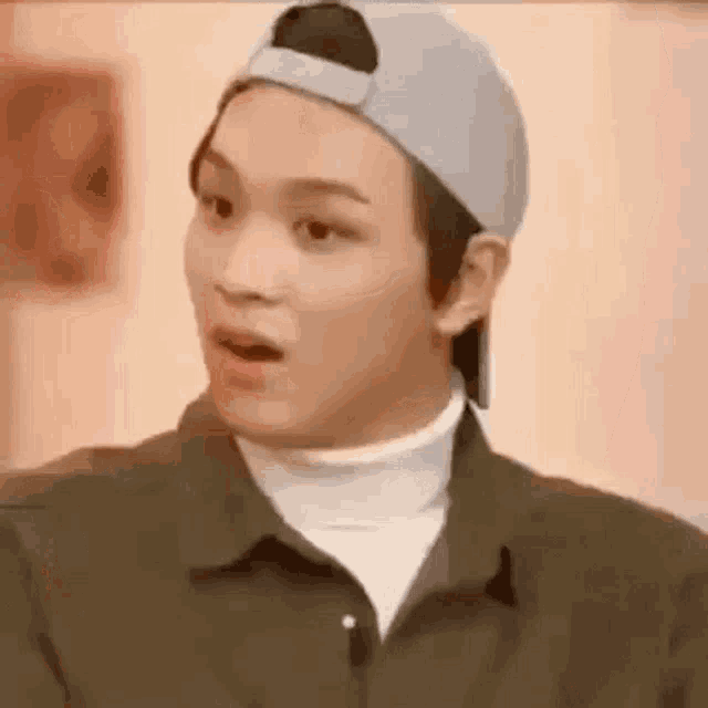 a young man wearing a baseball cap and a turtleneck is making a funny face .