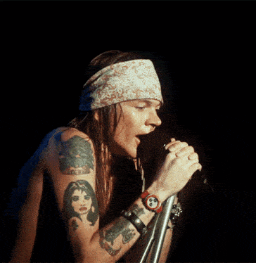 a man with tattoos on his arm singing into a microphone with a watch on his wrist that says ' rolex '