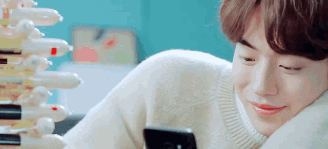 a young man in a white sweater is looking at a cell phone