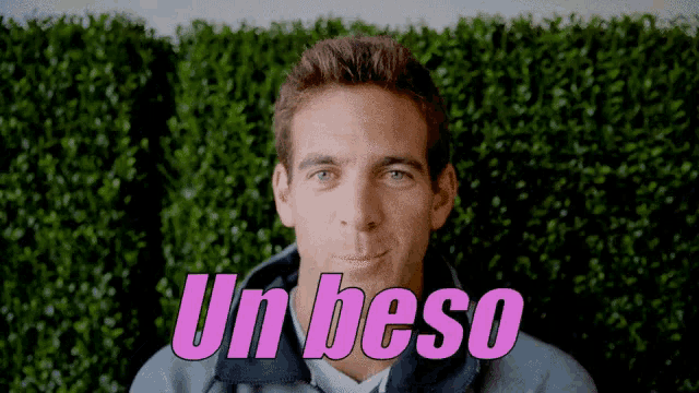 a man in front of a hedge with the word un beso in pink letters