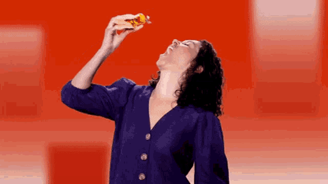 a woman in a purple shirt is eating a sandwich
