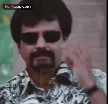 a man with a beard wearing sunglasses and a watch is giving the middle finger .