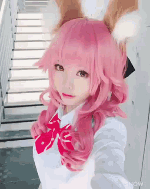 a girl with pink hair and fox ears is taking a selfie in front of some stairs .
