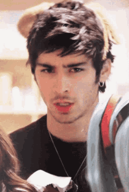 a young man wearing a black shirt and earrings looks at the camera