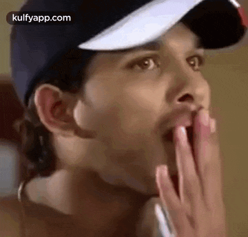 a close up of a man wearing a baseball cap with his hand on his mouth .