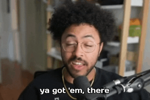 a man with glasses and an afro is talking into a microphone and saying `` ya got em , there '' .