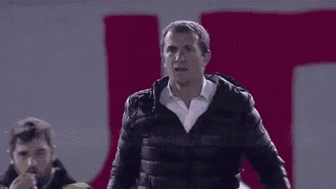a man wearing a black jacket and a white shirt is standing in front of a pink wall .
