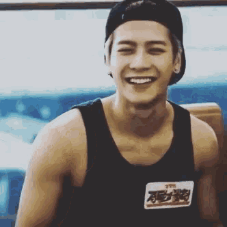 a young man wearing a black tank top and a hat is smiling .