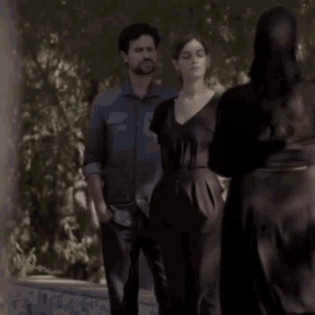 a woman in a black dress is standing next to a man in a denim shirt