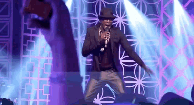 a man in a hat is singing into a microphone on stage .