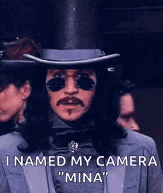 a man in a top hat and sunglasses says i named my camera " mina "