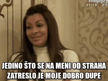 a woman is sitting in front of a wall and smiling while talking in a foreign language .