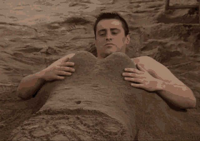 a shirtless man is buried in the sand with his hands on his stomach
