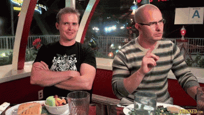 two men are sitting at a table in front of a sign that says a