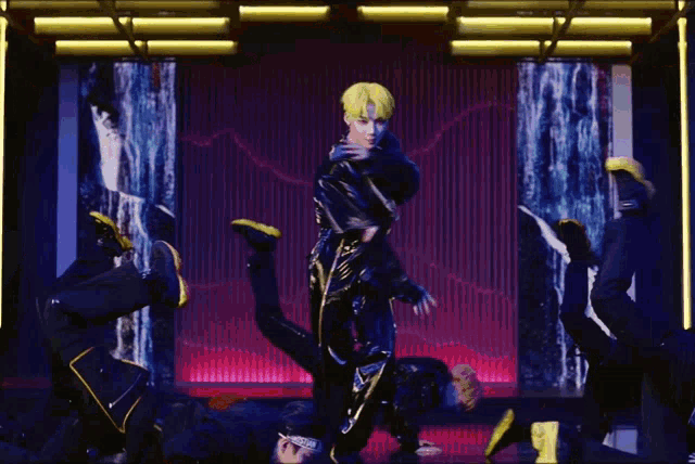 a man with yellow hair is dancing on a stage with other dancers