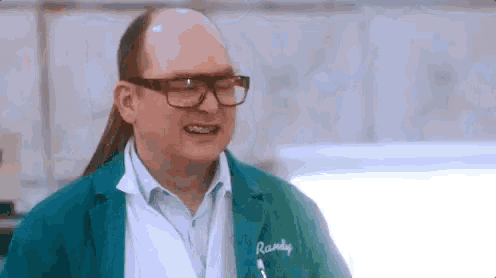 a bald man wearing glasses and a ponytail is making a funny face in a kitchen .