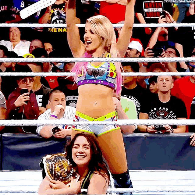 a woman in a wrestling ring holds up her arms in front of a crowd that is watching a wrestling match