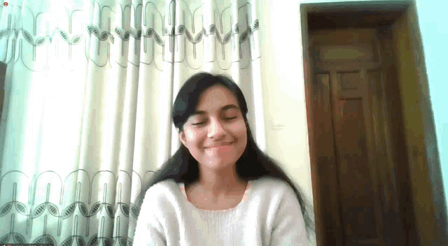 a woman is smiling with her eyes closed in front of a white curtain