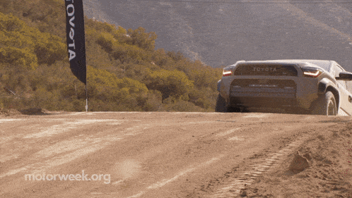 a toyota truck is driving down a dirt road next to a toyota flag