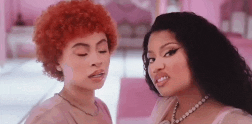 two women are standing next to each other in a pink room . one of the women has red hair and the other has black hair .