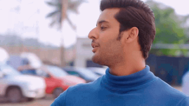 a man wearing a blue turtleneck sweater stands in front of a parking lot