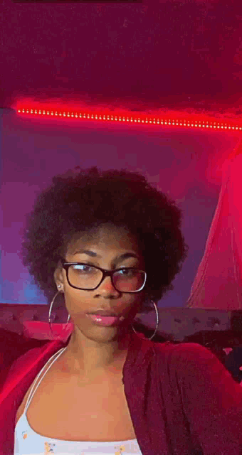 a young woman wearing glasses and hoop earrings is taking a selfie in front of a red light .
