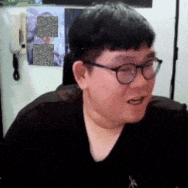 a man wearing glasses is sitting in front of a wall with a picture of a man on it