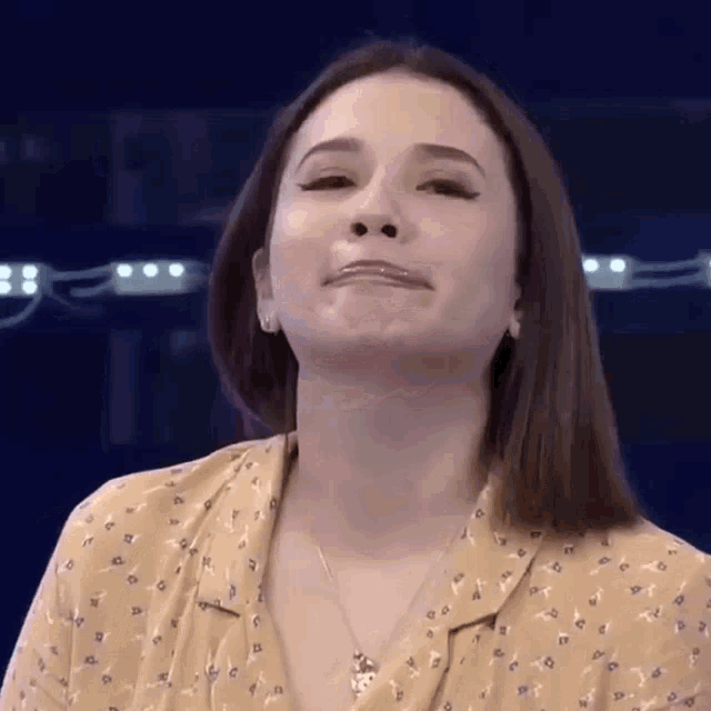 a woman wearing a yellow shirt and a necklace is making a face .
