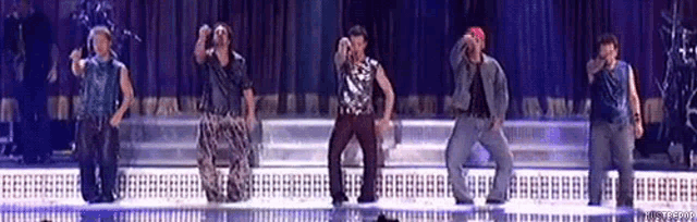 a group of young men are dancing on a stage and one of them is wearing a red hat