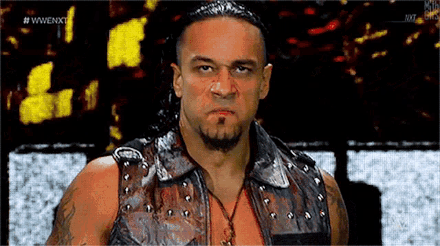 a man with a beard and a leather vest is standing in front of a sign that says wwe nxt .