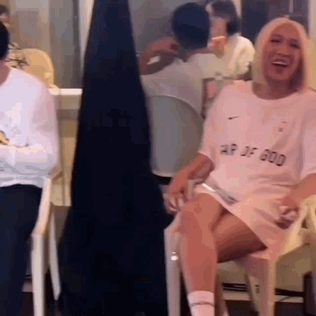 a woman is sitting in a chair with her legs crossed and wearing a white shirt that says air of god on it .