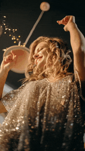 a woman in a sequined dress is dancing with her arms up