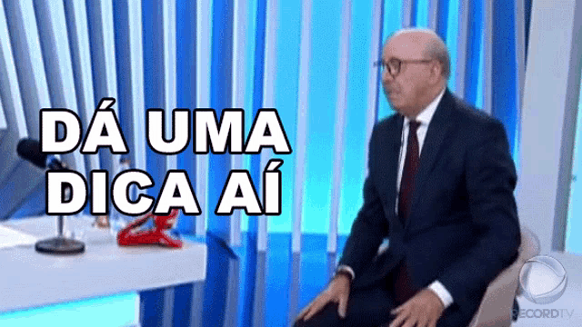 a man in a suit and tie is sitting in front of a microphone with the words " da uma dica ai " written above him