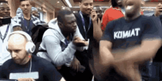 a man wearing a kombat shirt is dancing in a crowd of people .
