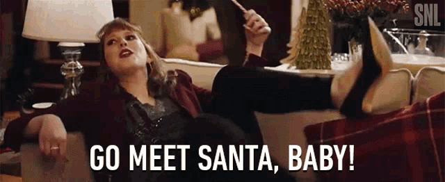 a woman is laying on a couch holding a wand and says `` go meet santa , baby '' .