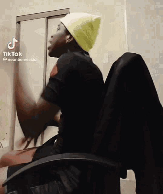 a man wearing a yellow beanie is sitting in a chair and making a funny face .