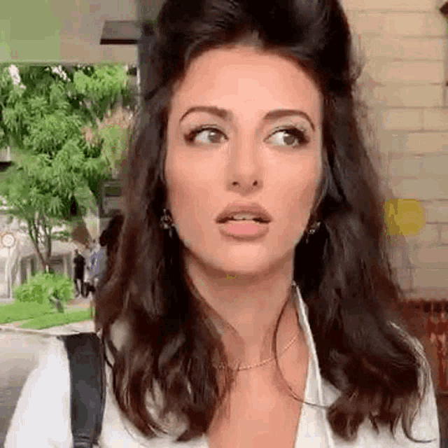 a woman with long dark hair is making a funny face while wearing a white shirt and a backpack .