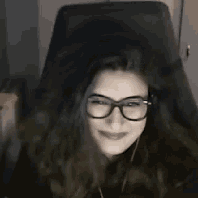 a woman is sitting in a chair wearing glasses and smiling .