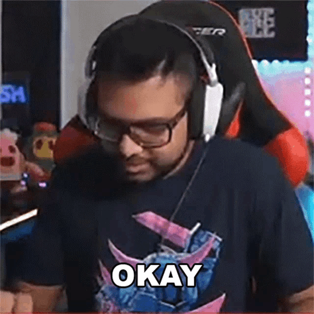 a man wearing headphones and glasses says okay while sitting in a gaming chair .