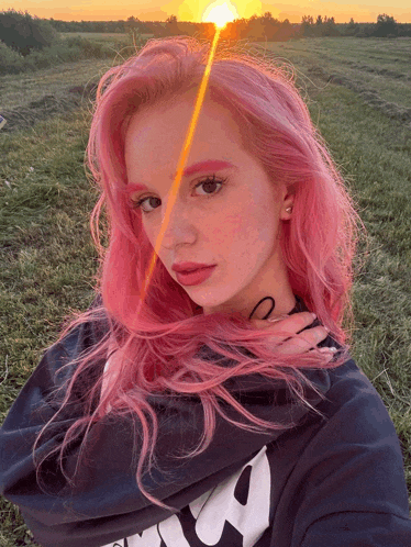 a girl with pink hair is standing in a field with the sun shining on her face