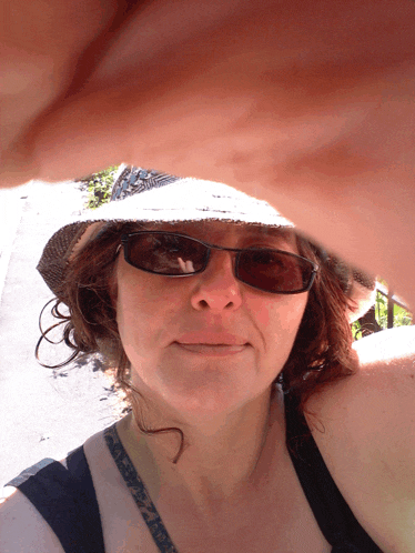 a woman wearing a hat and sunglasses takes a picture of herself