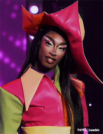 a drag queen is wearing a colorful outfit and hat