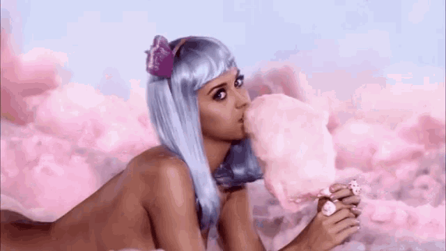 a naked woman in a blue wig is blowing a bubble of cotton candy .